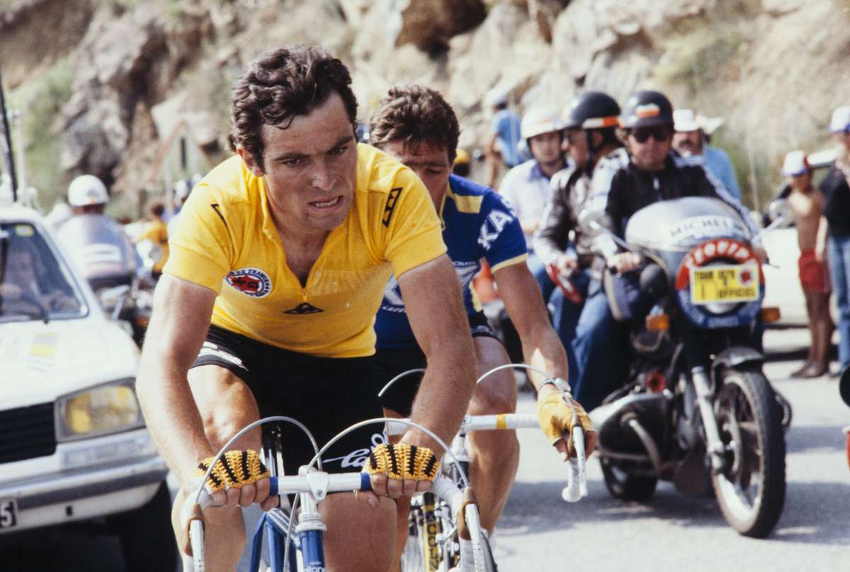 Bernard Hinault celebrating on the Tour de France podium with winner's bouquet and yellow jersey